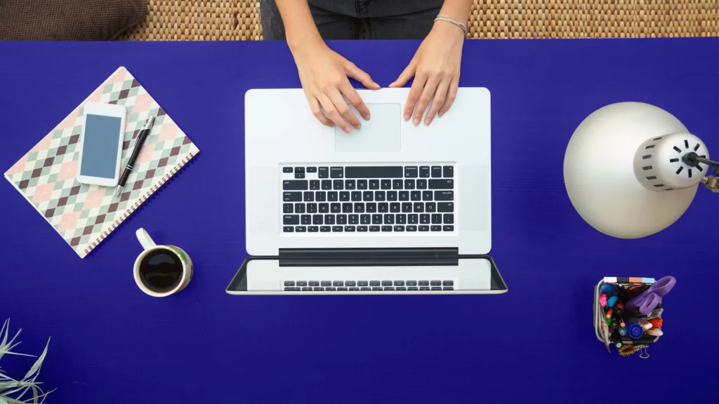 Layer of post "Maximizing the Impact of Direct Mail in a Digital World": A laptop seen from the top on a blue table with desk items around it, conveying a sense of organization and focus on work.