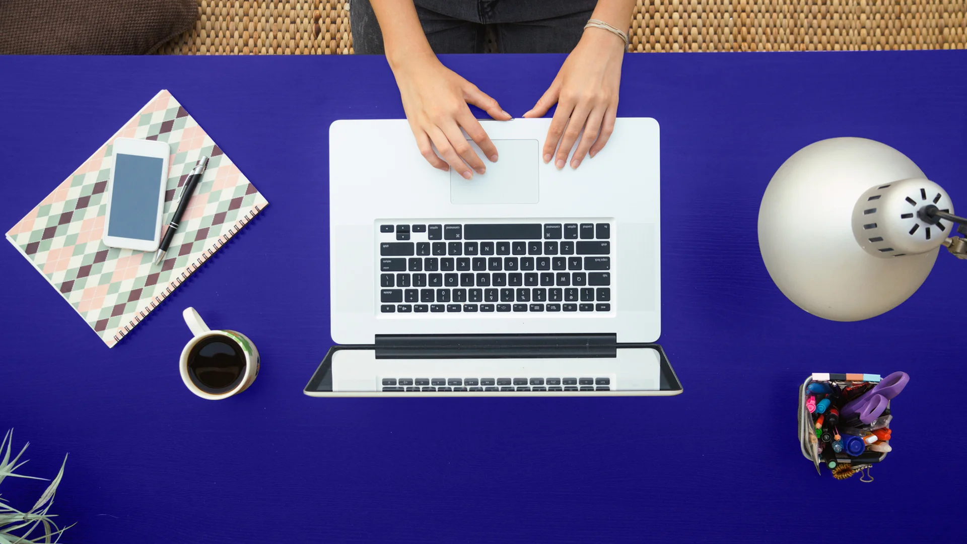 Layer of post "Maximizing the Impact of Direct Mail in a Digital World": A laptop seen from the top on a blue table with desk items around it, conveying a sense of organization and focus on work.